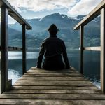 man in black hoodie sitting on wooden dock during daytime